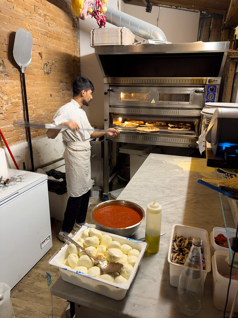 A young man makes pizza in a pizzaria restaurant in Florence, Italy.