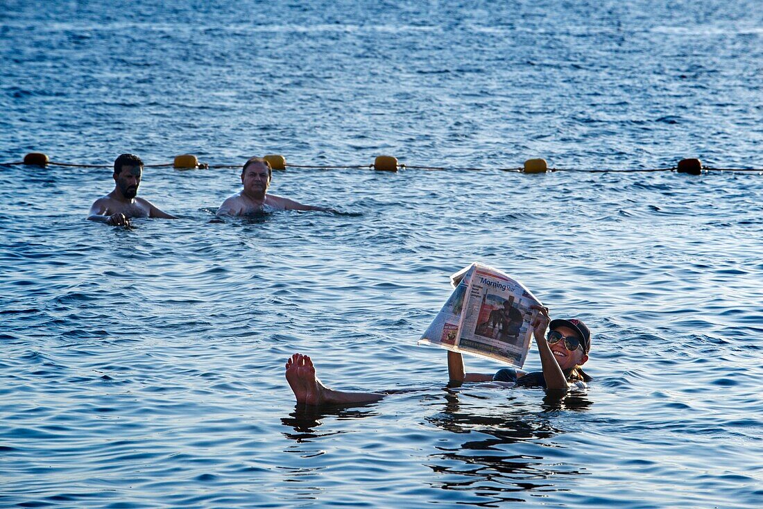 Junge Frau schwimmt und liest eine Zeitschrift im Toten Meer, Jordanien