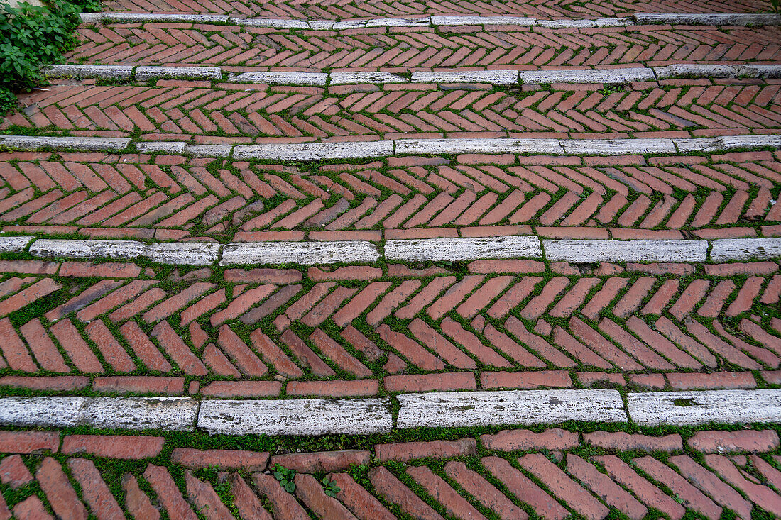 Ein Gehweg mit einem Fischgrätenmuster aus farbigen Steinen in der mittelalterlichen Stadt San Gimignano, Italien.