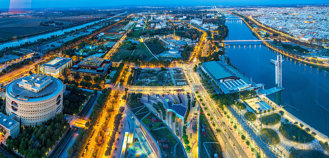 Discover the beauty of Cartuja Island in Seville, with Torre Triana illuminated at dusk between the Guadalquivir River's arms.