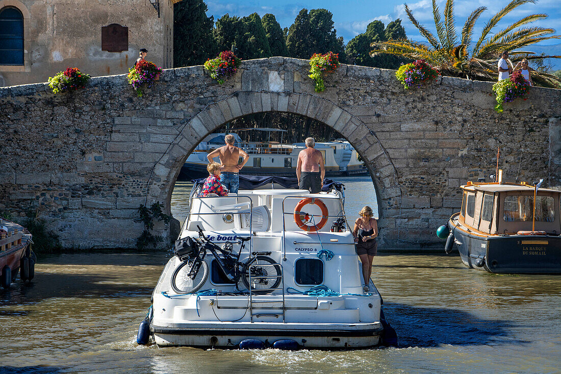 Canal du Midi an Brücke und Dorf Le Somail Aude Südfrankreich Südliche Wasserstraße Wasserstraßen Urlauber stehen Schlange für eine Bootsfahrt auf dem Fluss, Frankreich, Europa