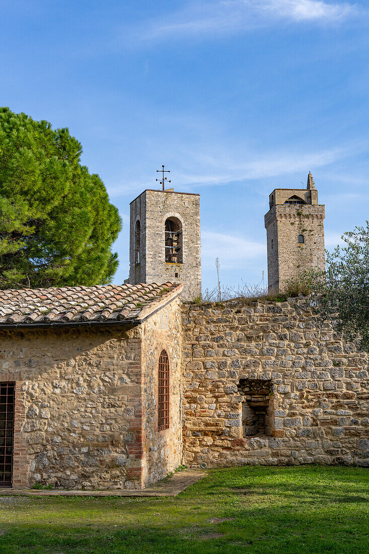 Der Glockenturm der Kathedrale, Torre Grossa, und die Ruinen einer mittelalterlichen Festung in der ummauerten Stadt San Gimignano, Italien. Die Ruinen umschließen den Parco della Rocca.