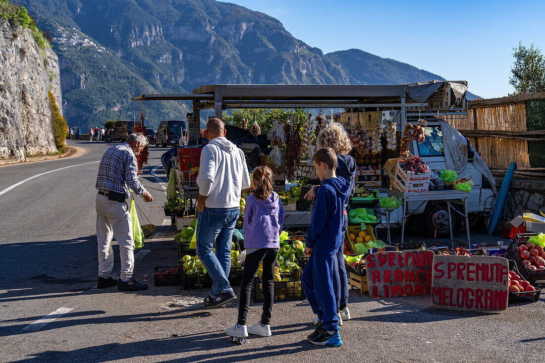 Ein Straßenverkäufer, der einer Familie an der Straße zur Amalfiküste in der Nähe von Positano, Italien, frische Produkte verkauft.