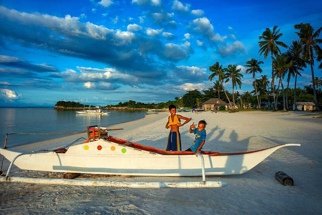 Local children and fish boats in white sand beach in of Langub Beach Malapascua island, Cebu, Philippines