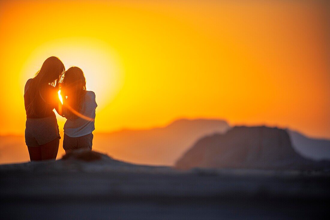 Zwei Touristinnen blicken bei Sonnenuntergang über den roten Sand der Wüste von Wadi Rum, Jordanien