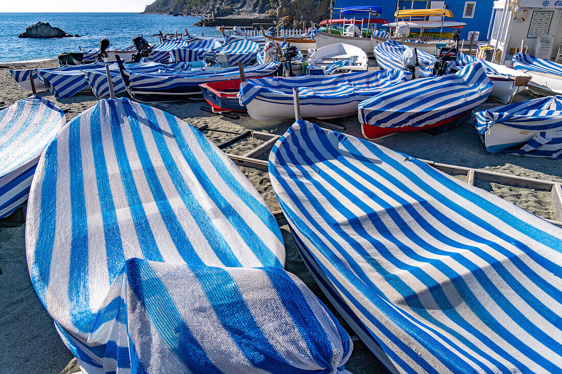 Boote mit gestreiften Planen am Strand in der Nebensaison in Monterosso al Mare, Cinque Terre, Italien.