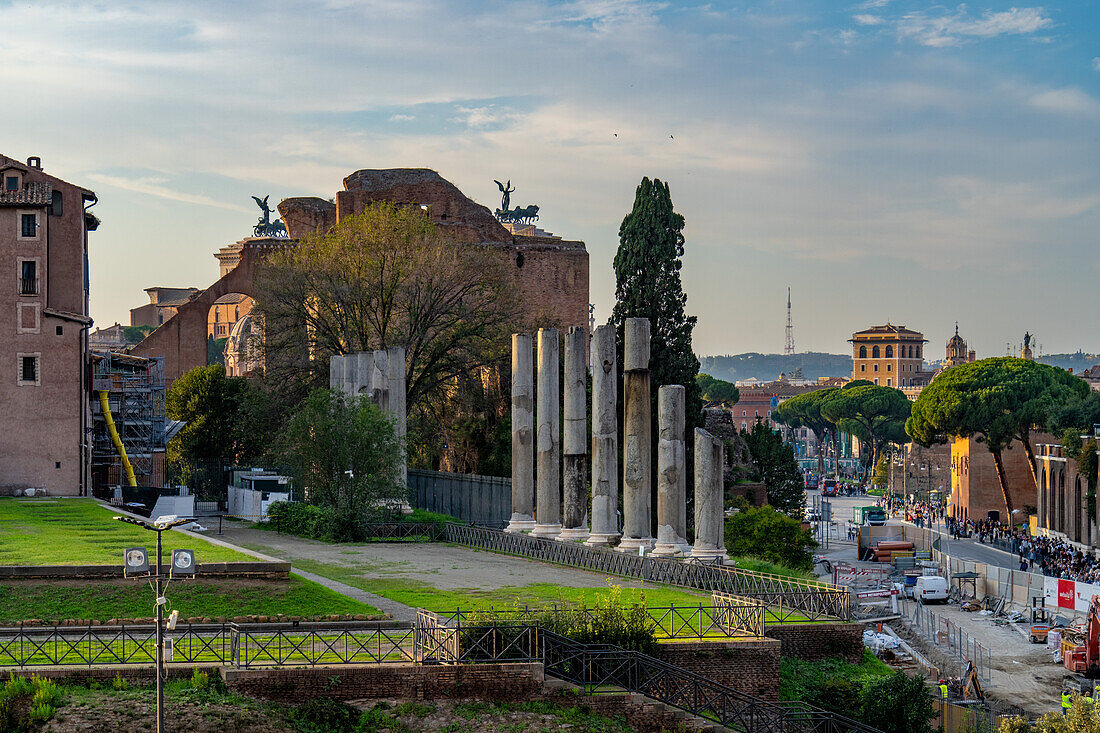 Roman pillars along the edge of the Temple of Venus and Roma in the Colosseum Archaeological Park. Rome, Italy. At right are crowds along the Via dei Fori Imperiali. Behind are the Winged VIctory statues on top of the Victor Emmanuel II Monument.