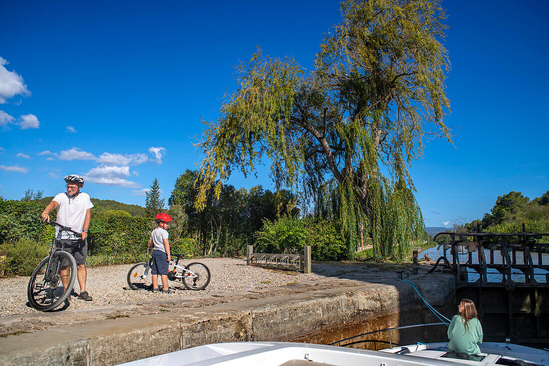 Bicycles and Boat crossing the Écluse de Pechlaurier look. Canal du Midi at village of Argens-Minervois Aude South of France southern waterway waterways holidaymakers queue for a boat trip on the river, France, Europe