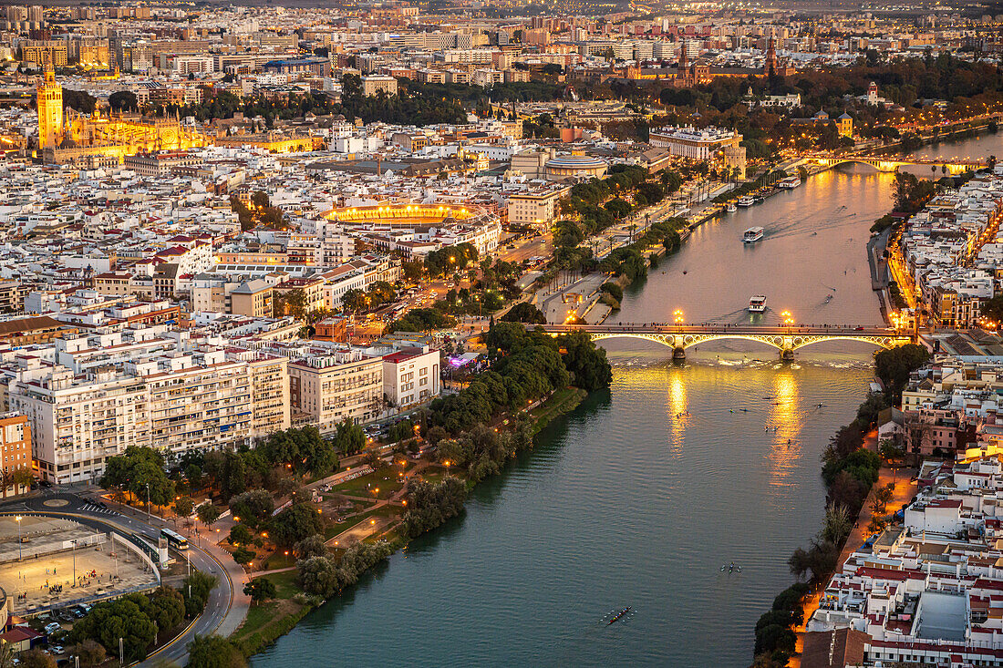 Spectacular aerial view showcasing Triana Bridge, the Cathedral, and Torre del Oro along the Guadalquivir River in Seville at sunset.