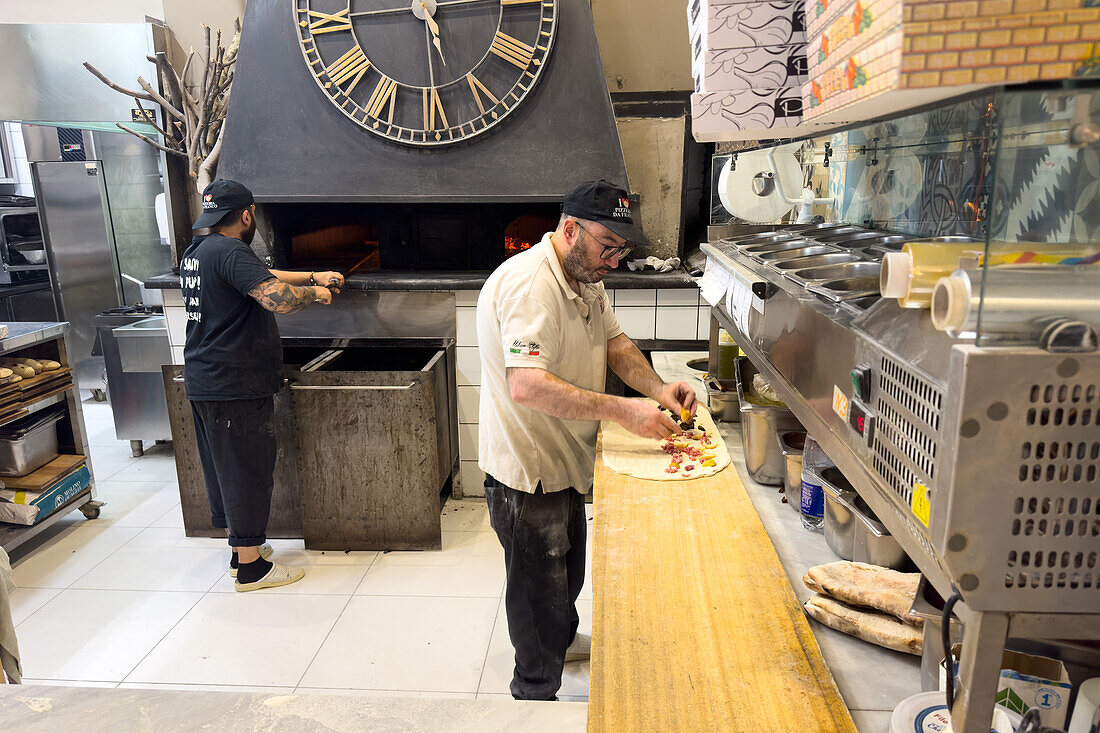 Ein Pizzaiolo oder Pizzabäcker bereitet eine Pizza in einer Pizzeria in Sorrento, Italien, zu.