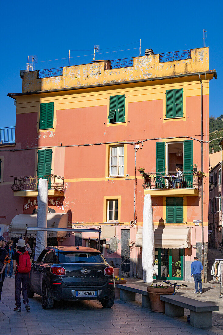 A woman sits on the balcony of a colorful building in Monterosso al Mare, Cinque Terre, Italy.