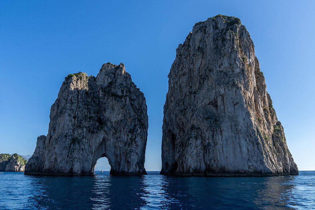 Die Farallons oder Faraglioni, Meeresfelsen vor der Küste der Insel Capri, Italien. L-R: Mezzo, mit einem Boot, das durch den Meeresbogen sichtbar ist, und Scopolo oder Fuori.