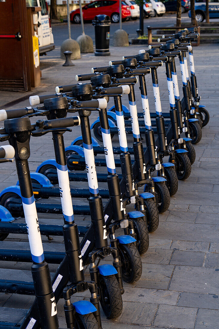 A row of rechargeable electric scooters for rent in front of the train station in La Spezia, Italy.