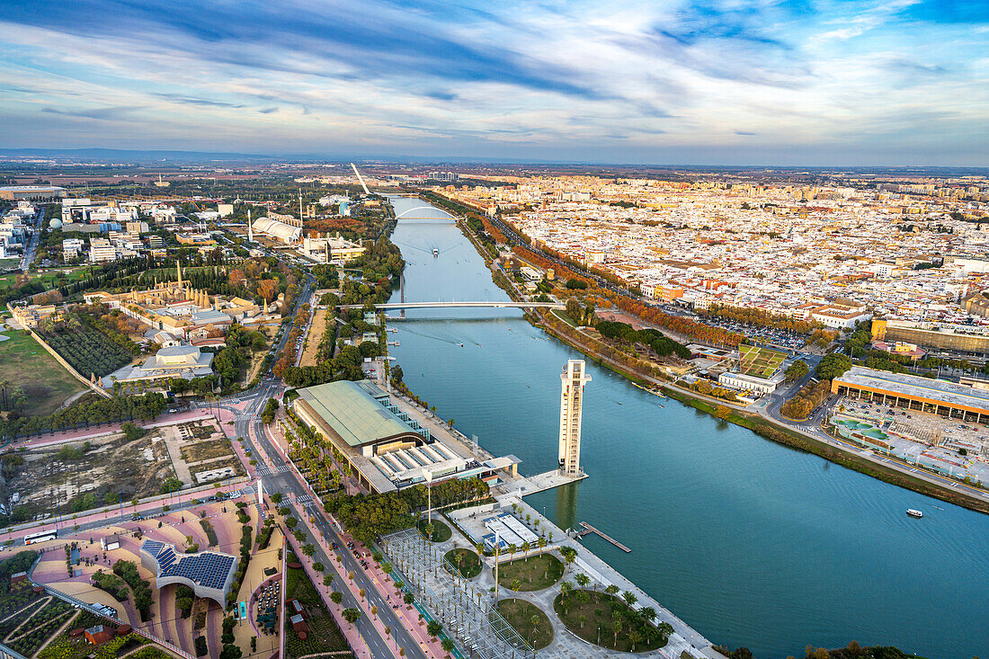 Spectacular panorama shows the Guadalquivir River and Seville's vibrant cityscape from the Mirador de la Torre Sevilla at sunset.