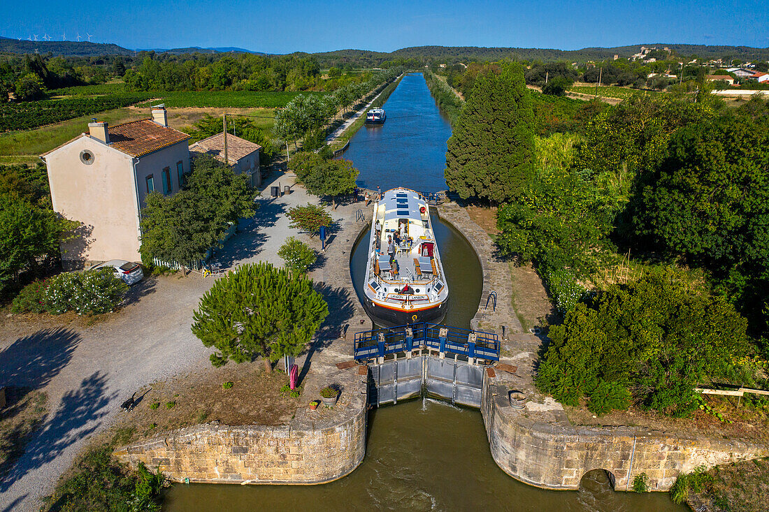 Luftaufnahme eines großen Bootes beim Überqueren der Écluse d'Argens argens Blick. Canal du Midi bei der Ortschaft Argens-Minervois Aude Südfrankreich Südliche Wasserstraße Wasserstraßen Urlauber stehen Schlange für eine Bootsfahrt auf dem Fluss, Frankreich, Europa