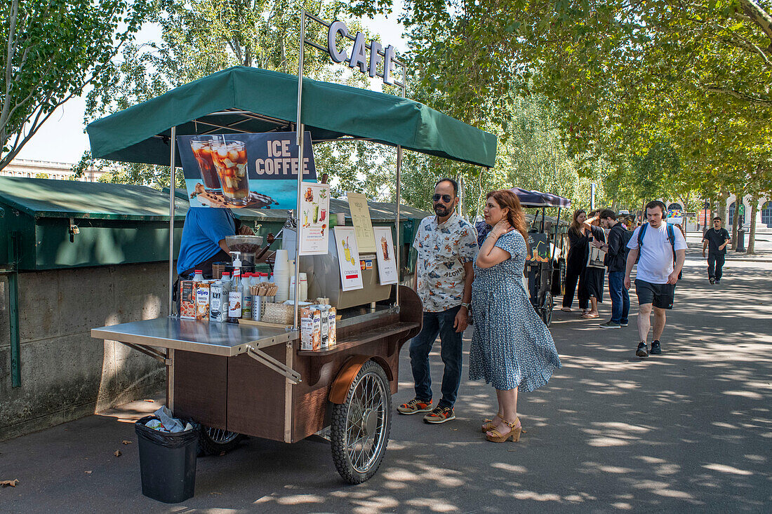 Eiskaffee-Stand neben den Bouquinistes oder Bücherständen entlang der Seine in Paris in der Nähe der Kathedrale Notre Dame, Riverside Bouquinistes, grüne Kästen, die Bücher aus zweiter Hand am Quai Malaquais am Ufer der Seine verkaufen.