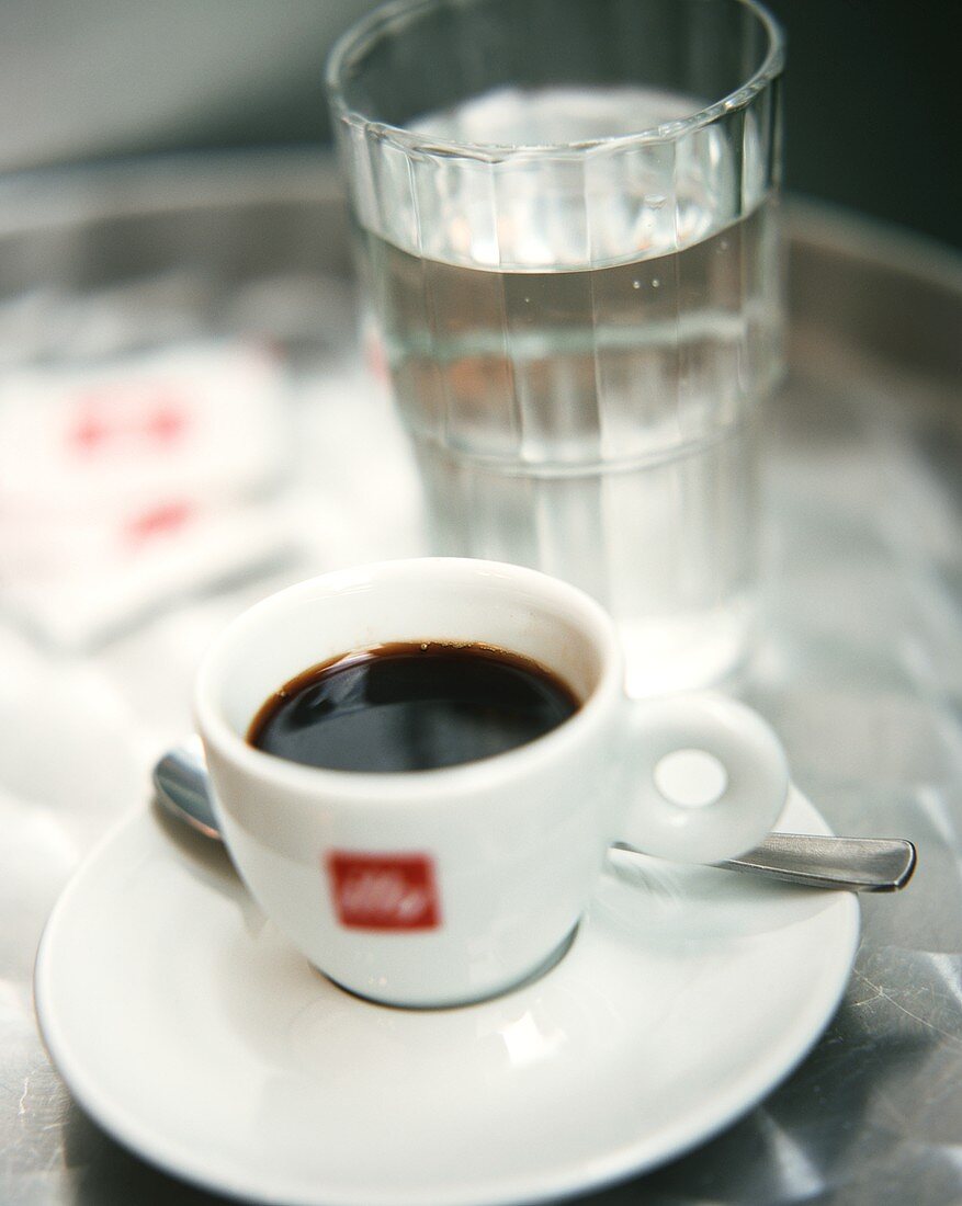 Eine Tasse Espresso und ein Glas Wasser auf Bistrotisch