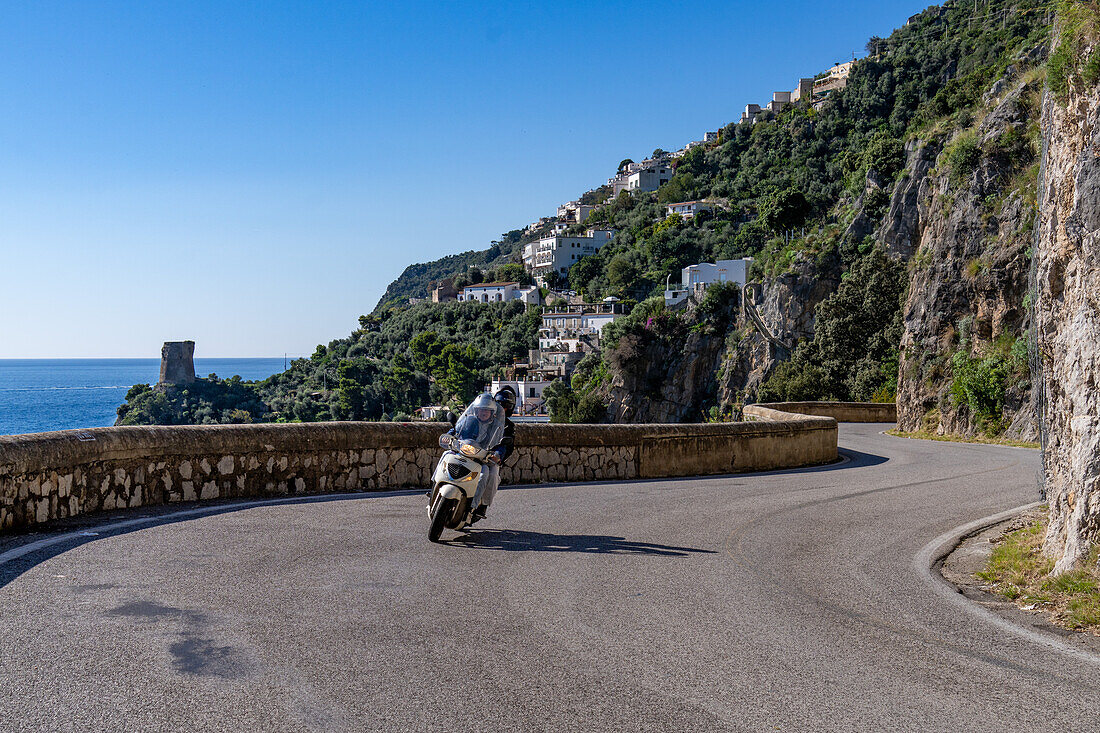 Torre a Mare, a Saracen tower and a motorcyclist on the winding Amalfi Coast road at Praiano, Italy.