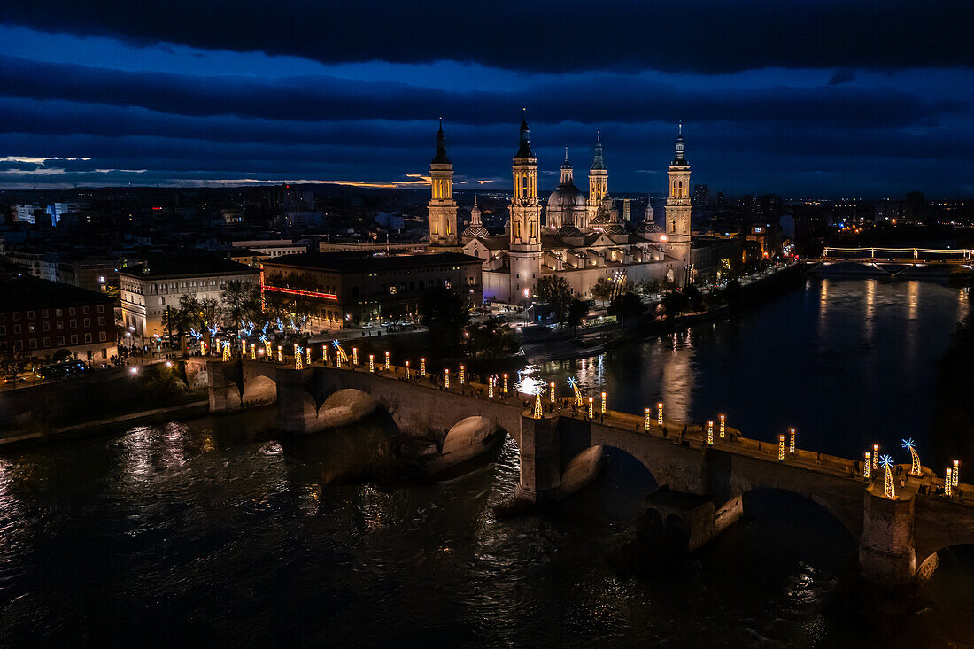 Aerial view of the Cathedral Basilica of Our Lady of the Pillar and Stone Bridge illuminated at night during Christmas, Zaragoza, Spain