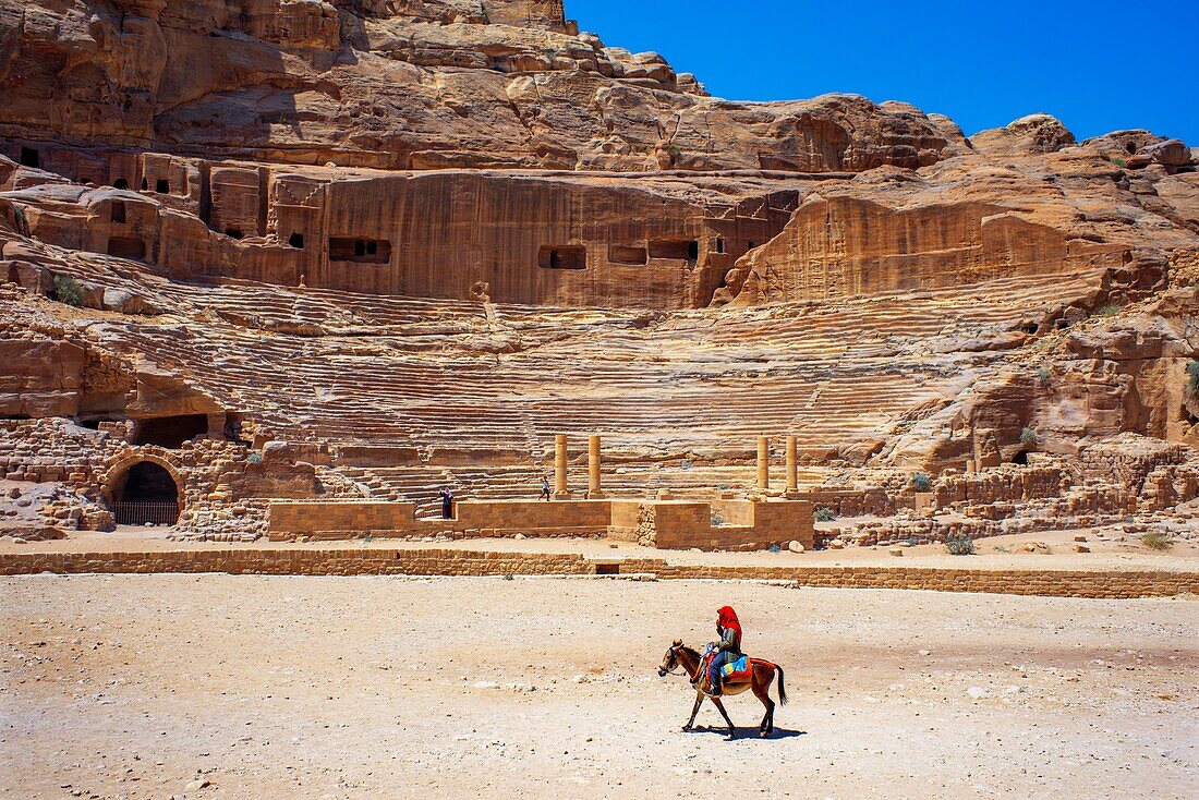 Römisches Theater in den Ruinen von Petra, Jordanien. Geschnitztes Amphitheater Theater Siq Petra Jordanien. Das Theater wurde von den Nabatäern 100 n. Chr. als Schatzkammer gebaut und von den Römern erweitert. Das Theater ist aus rotem Stein gefertigt und bietet Platz für bis zu 7.000 Personen. Beduinen auf einem Kamel vor dem Amphitheater von Petra.