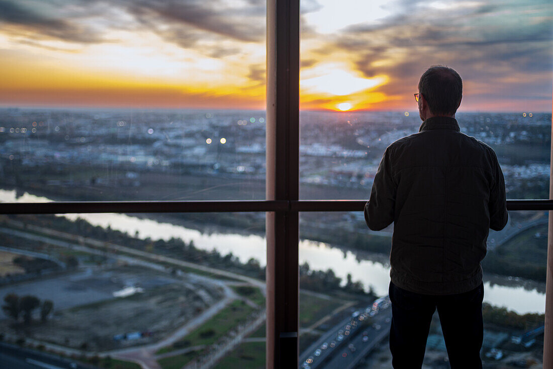 A person gazes at the breathtaking sunset over Seville from the observation deck of Torre Sevilla, capturing the beauty of the evening.