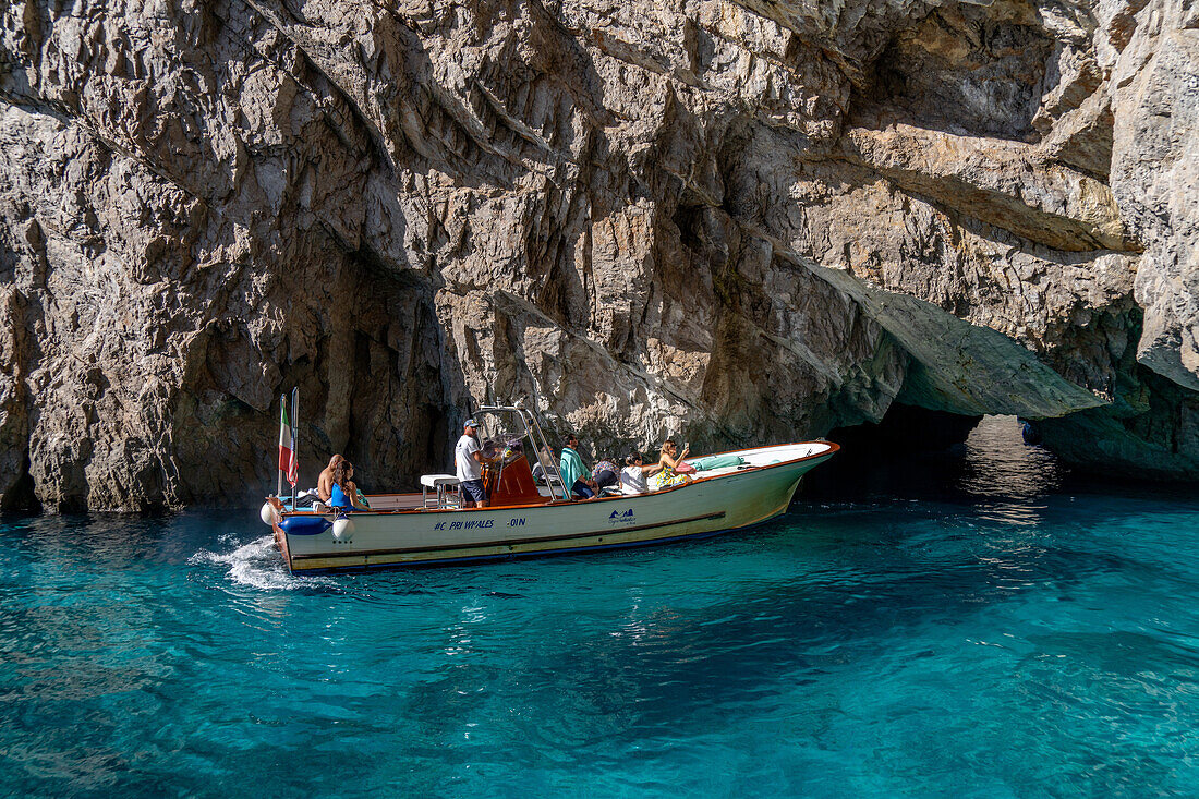 Menschen in einem Ausflugsboot im klaren grünen Wasser bei der Grünen Grotte an der Küste der Insel Capri, Italien.