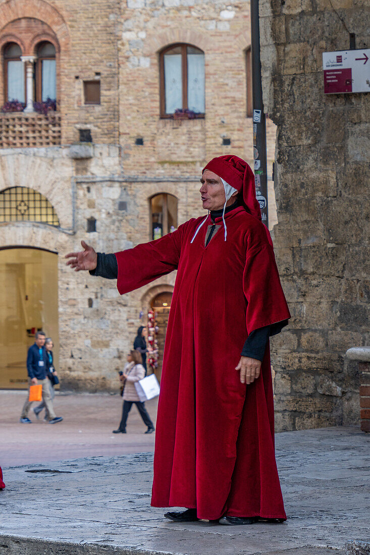 An actor in costume imitates Dante on the street in the medieval walled town of San Gimignano, Italy.