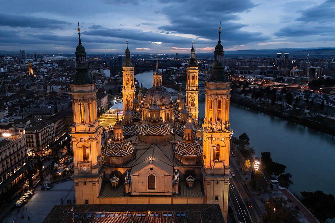 Luftaufnahme der Kathedralenbasilika Unserer Lieben Frau von der Säule und des nachts beleuchteten Platzes El Pilar während der Weihnachtszeit, Zaragoza, Spanien