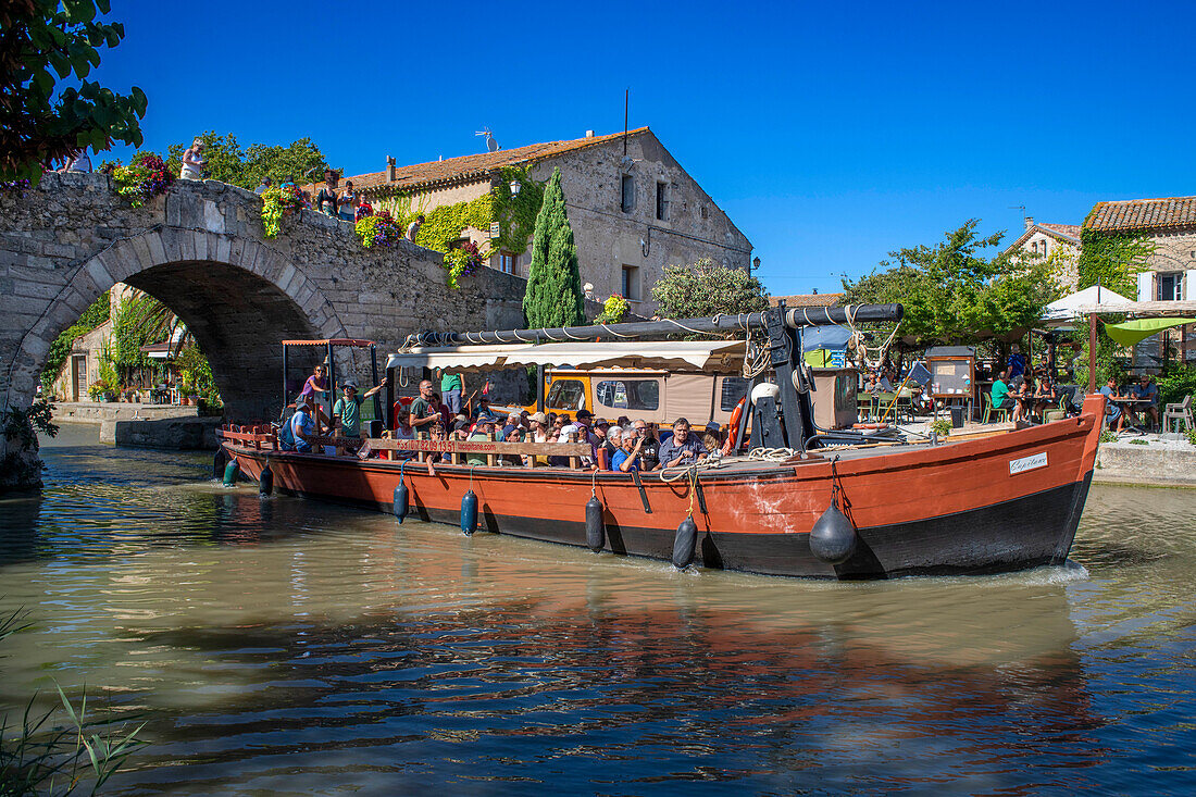 Canal du Midi an Brücke und Dorf Le Somail Aude Südfrankreich Südliche Wasserstraße Wasserstraßen Urlauber stehen Schlange für eine Bootsfahrt auf dem Fluss, Frankreich, Europa