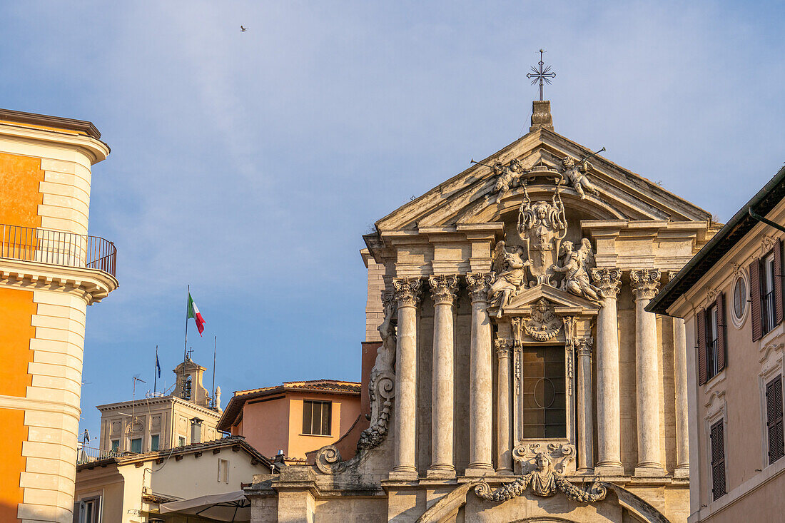 Fassade der Kirche der Heiligen Vinzenz und Anastasio auf der Piazza di Trevi in Rom, Italien. Links ist die italienische Flagge auf dem Turm des Quirinalspalastes, der offiziellen Residenz des italienischen Staatspräsidenten, zu sehen.