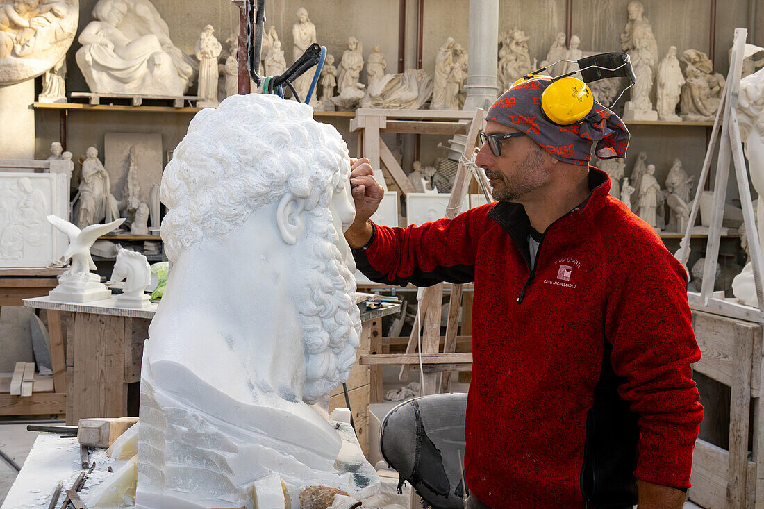 Ein Bildhauer arbeitet an einer teilweise fertigen Büste des Herkules in einem Marmorschnitzatelier in Carrara, Italien. Das Original befindet sich in der Sammlung Farnese in Neapel.