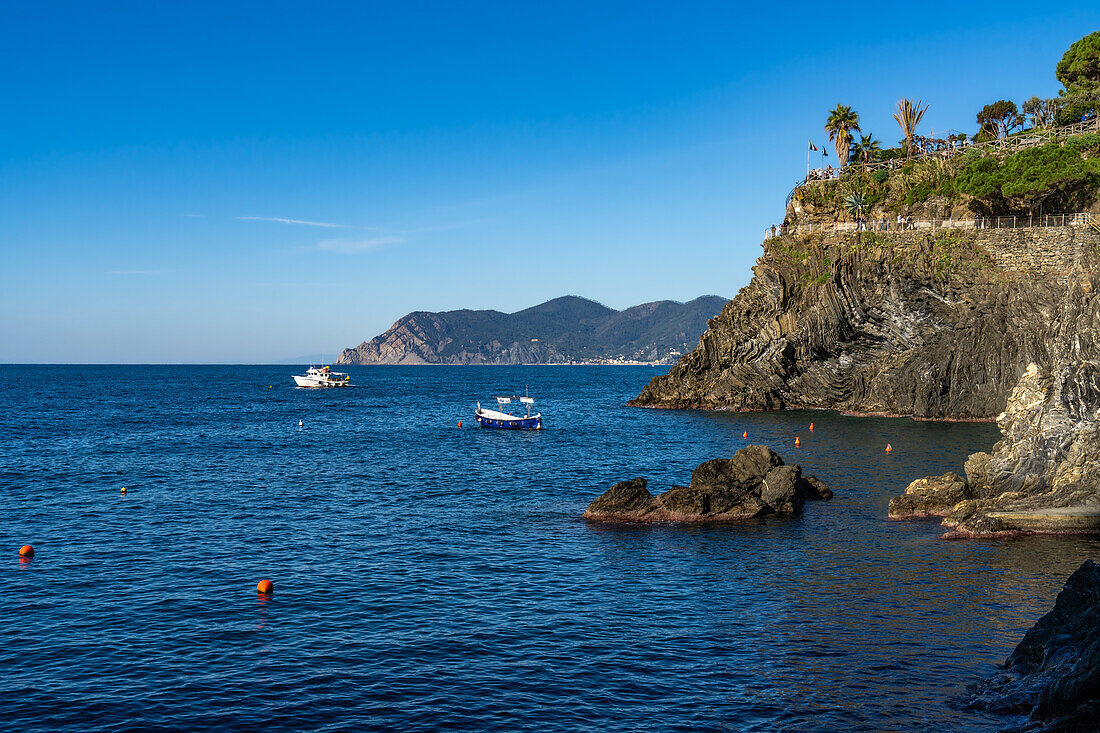 Fischerboote vor der zerklüfteten Küste der Stadt Manarola in den Cinque Terre, Italien. Touristen befinden sich auf einem Aussichtspunkt rechts.