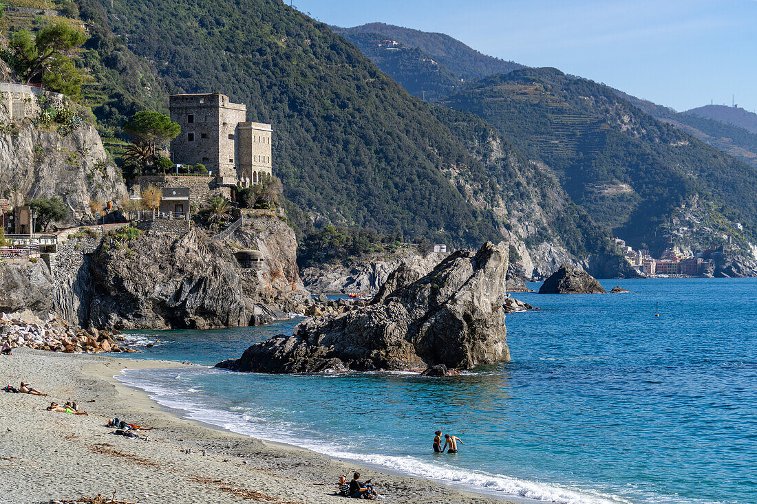 Touristen am Strand außerhalb der Hauptsaison in Monterosso al Mare, Cinque Terre, Italien. Dahinter befindet sich der Malpasso-Felsen.