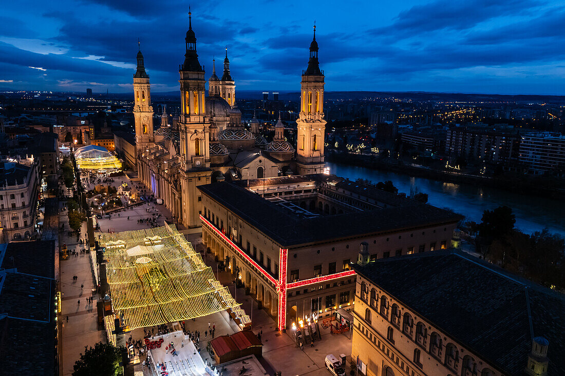 Luftaufnahme der Kathedralenbasilika Unserer Lieben Frau von der Säule und des nachts beleuchteten Platzes El Pilar während der Weihnachtszeit, Zaragoza, Spanien