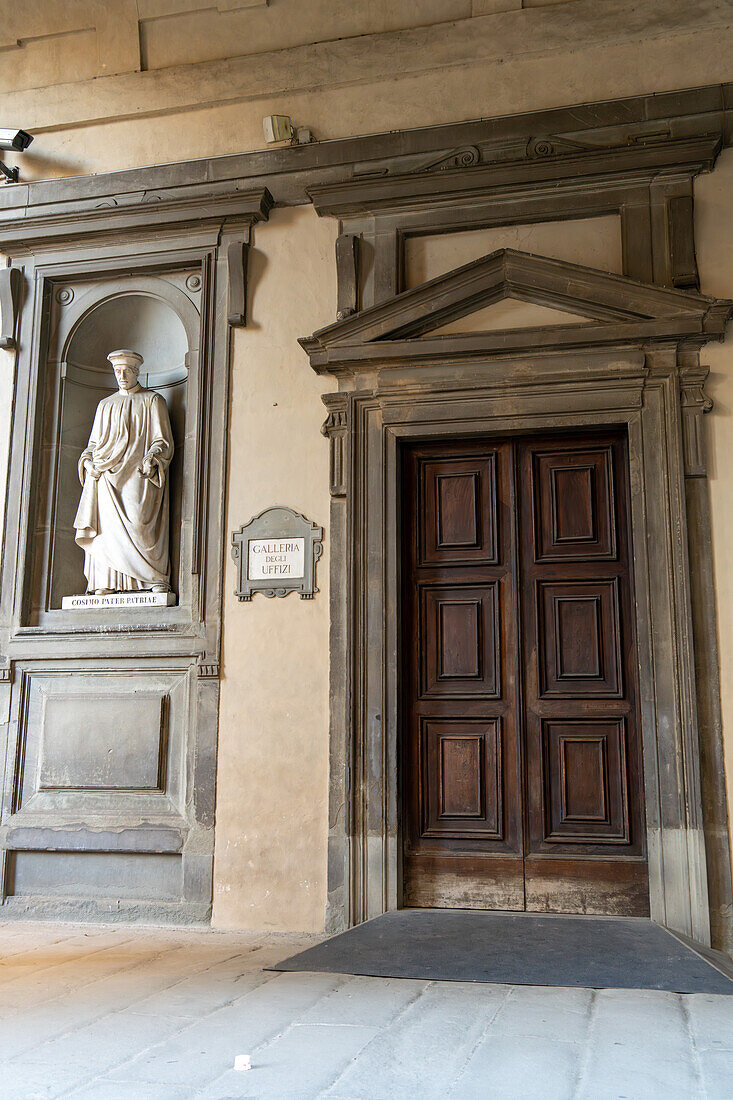 Eine Statue von Cosimo I. de' Medici neben einem Schild und dem Eingang zur Uffizien-Galerie in Florenz, Italien. Das Gebäude wurde 1560 von Cosimo I. in Auftrag gegeben.