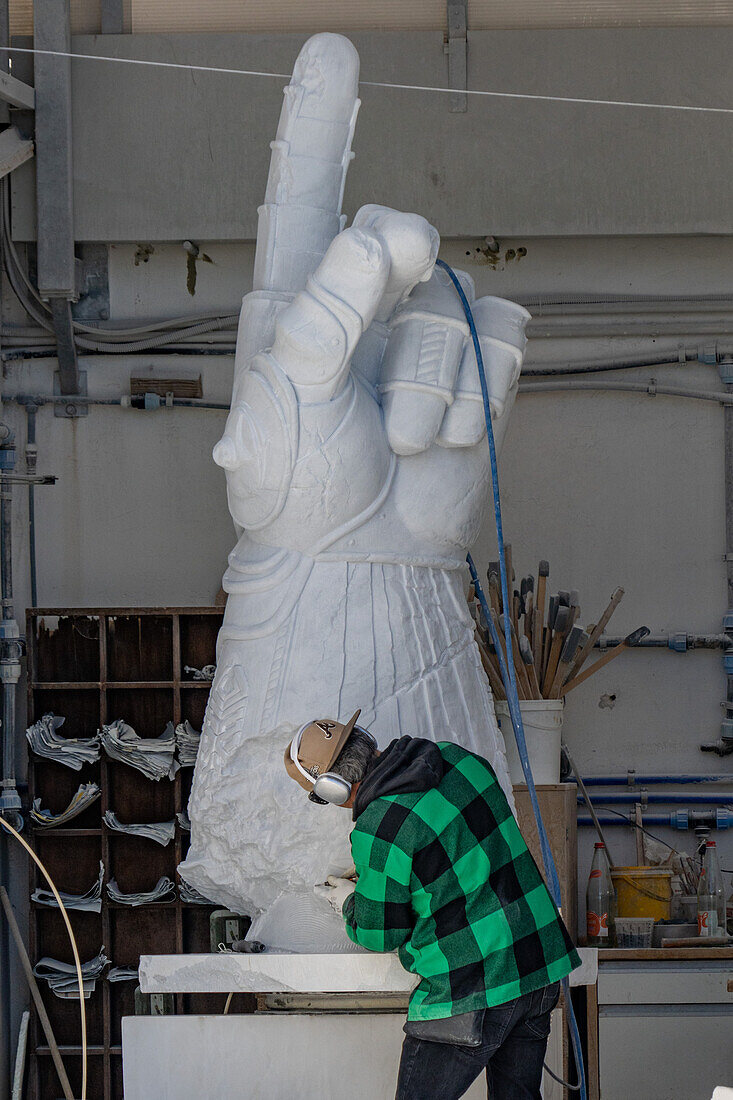 A sculptor uses a pneumatic chisel to carve a marble statue in a carving studio in Fantscritti, Carrara, Italy.