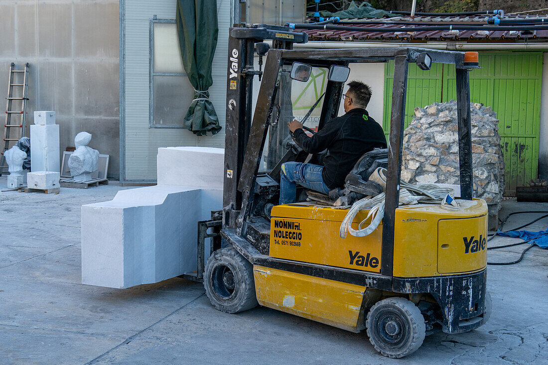 A worker at a marble carving studio moves a block of cut marble with a forklift. Fantiscritti, Carrara, Italy.