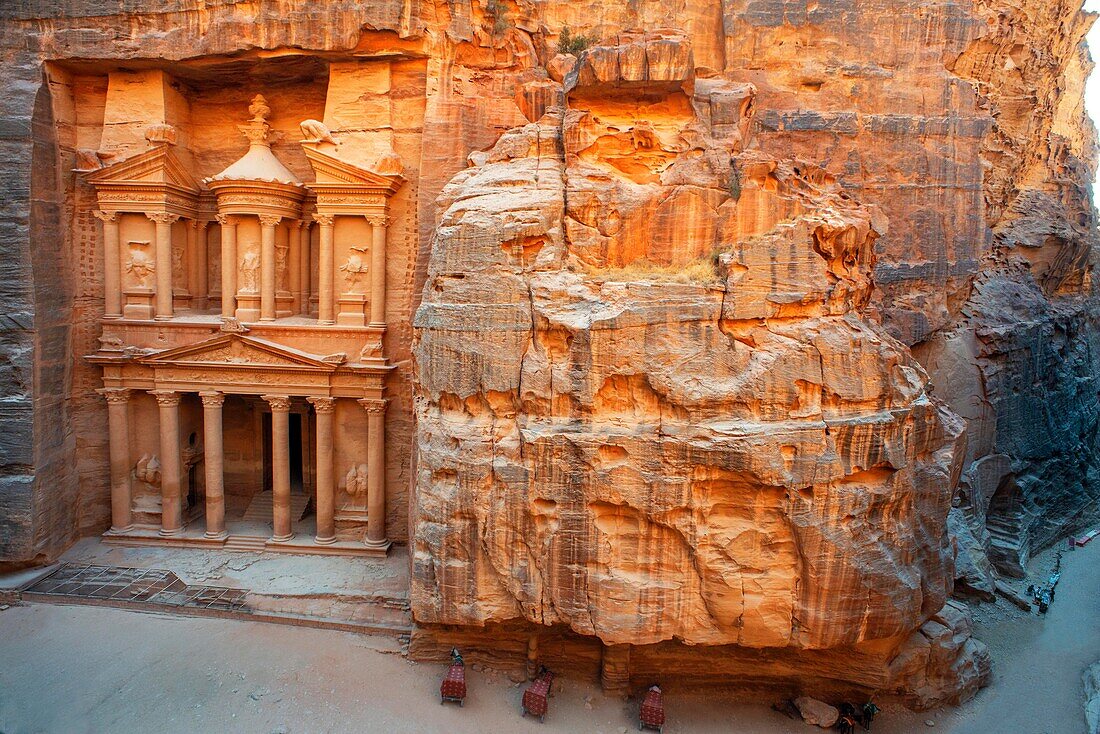 Die Schatzkammer, El Khazneh, Petra, Jordanien. Petra ist eine historische und archäologische Stadt im südjordanischen Gouvernement Ma'an, die für ihre in Felsen gehauene Architektur und ihr Wasserleitungssystem bekannt ist. Aufgrund der Farbe des Steins, aus dem sie gemeißelt ist, wird Petra auch als Rosenstadt bezeichnet. Sie wurde möglicherweise bereits 312 v. Chr. als Hauptstadt der Nabatäer gegründet und ist ein Symbol für Jordanien sowie die meistbesuchte Touristenattraktion des Landes. Sie liegt am Hang des Jebel al-Madhbah (von einigen als der biblische Berg Hor identifiziert) in einem