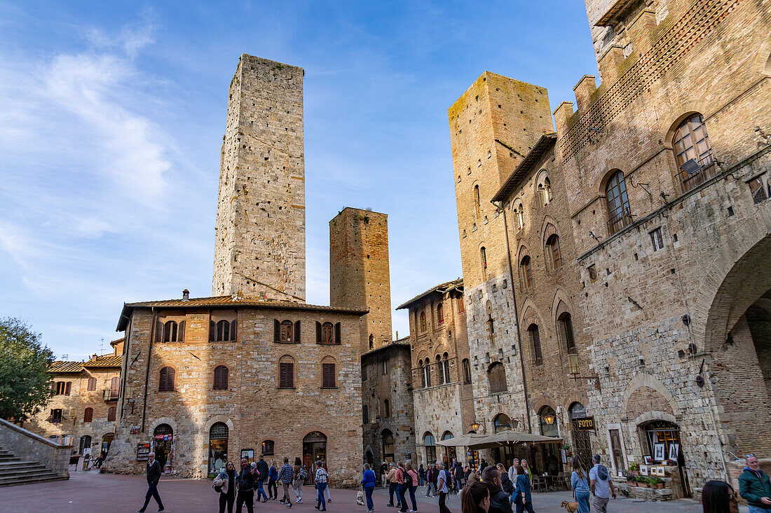 Tourists on the Piazza del Duomo with its towers in the medieval walled city of San Gimignano, Italy. L-R: Torri Salvucci, Torre Pettini and Torre Chigi.