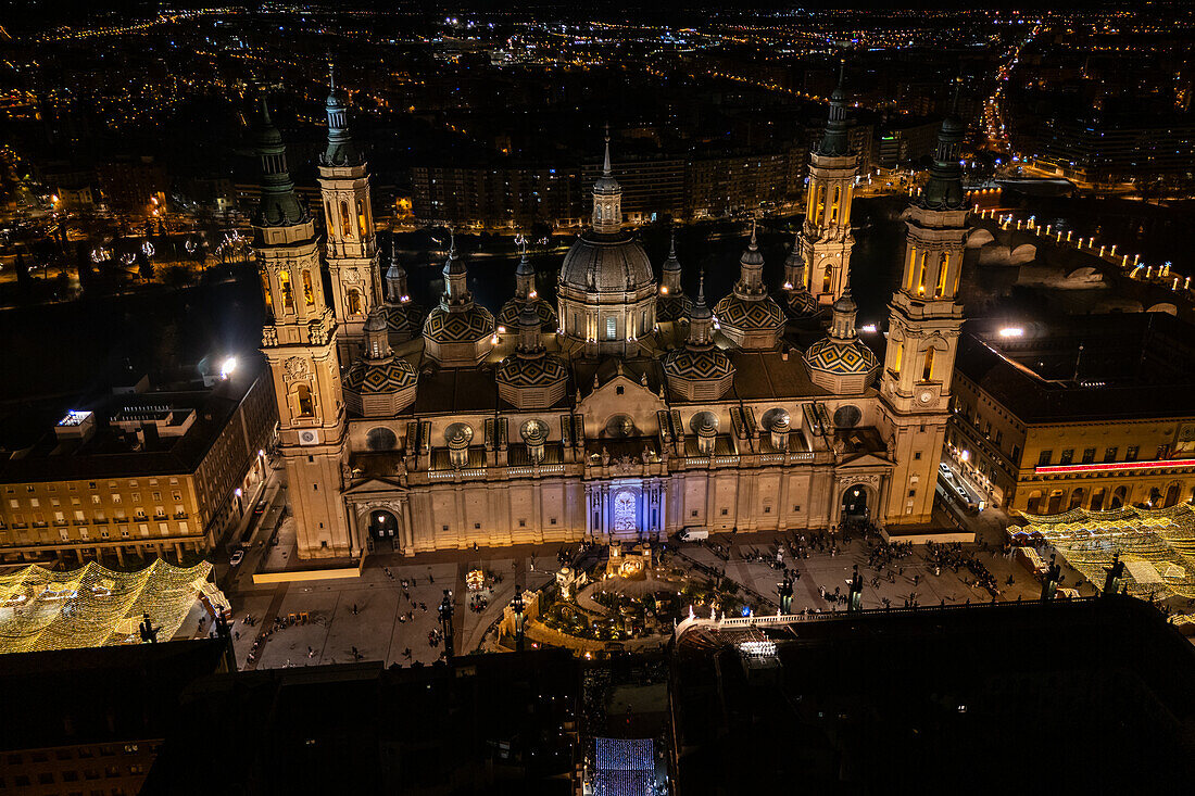 Luftaufnahme der Kathedralenbasilika Unserer Lieben Frau von der Säule und des nachts beleuchteten Platzes El Pilar während der Weihnachtszeit, Zaragoza, Spanien