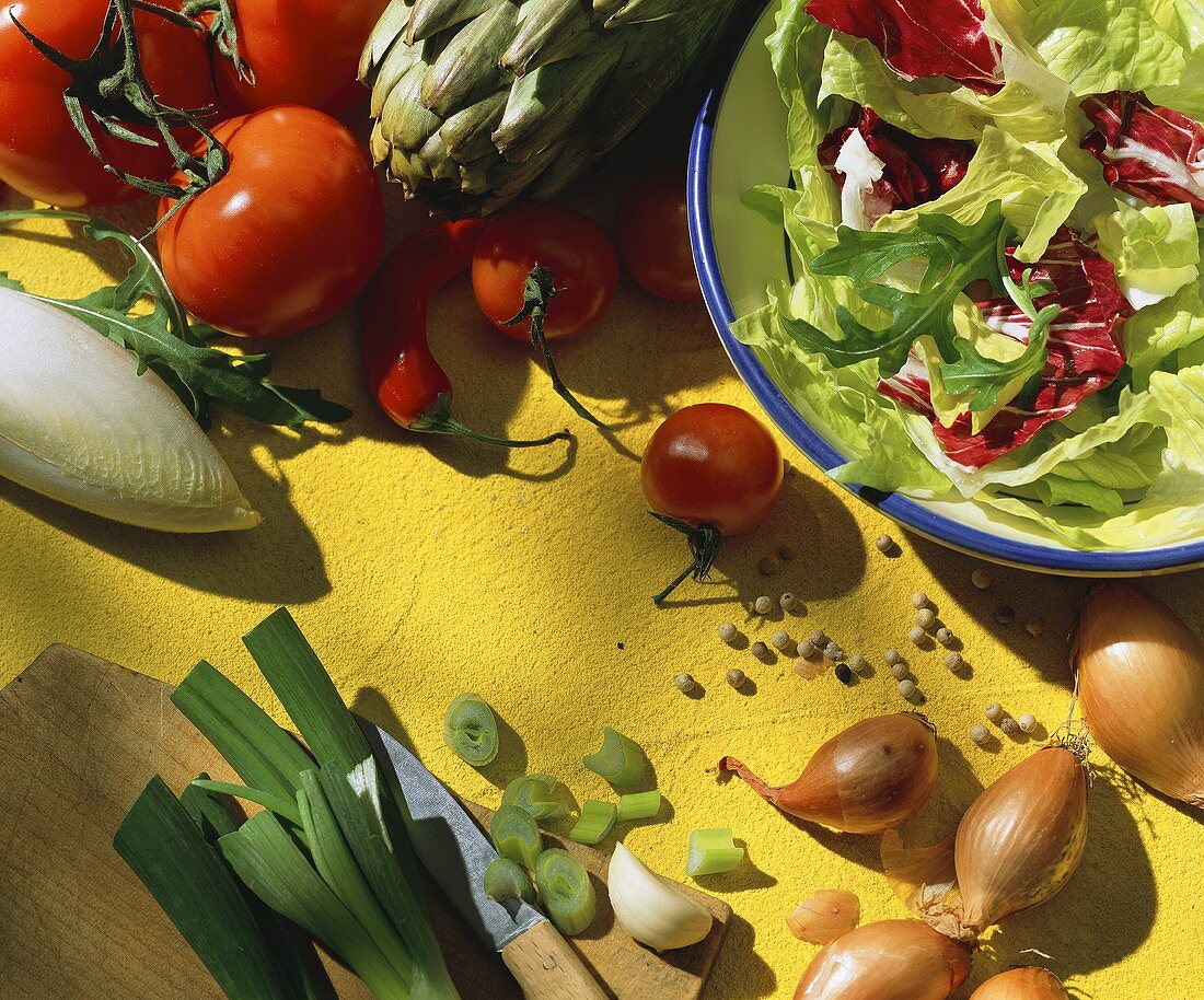 Stillleben mit Blattsalaten und Gemüse auf gelbem Untergrund
