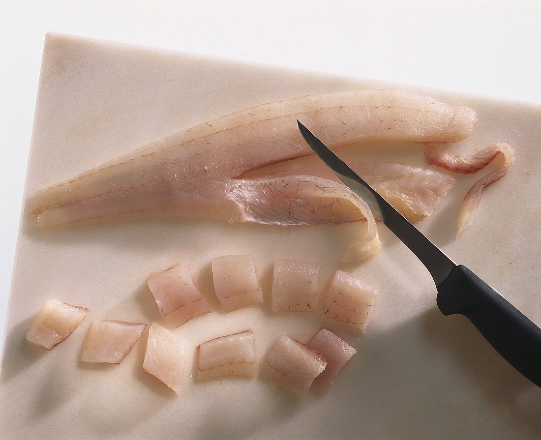Pike-perch fillet, partly cut into pieces, with knife