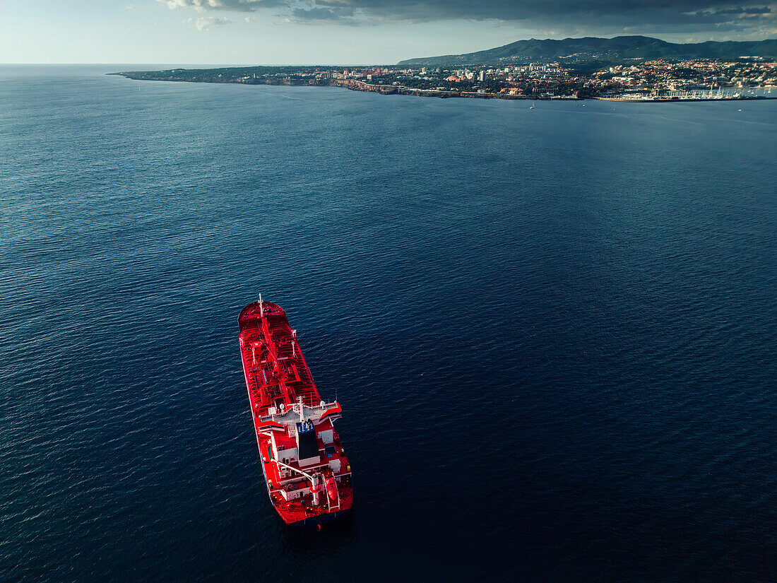 A large red cargo ship in calm waters, close to the shoreline of a coastal city, Portugal