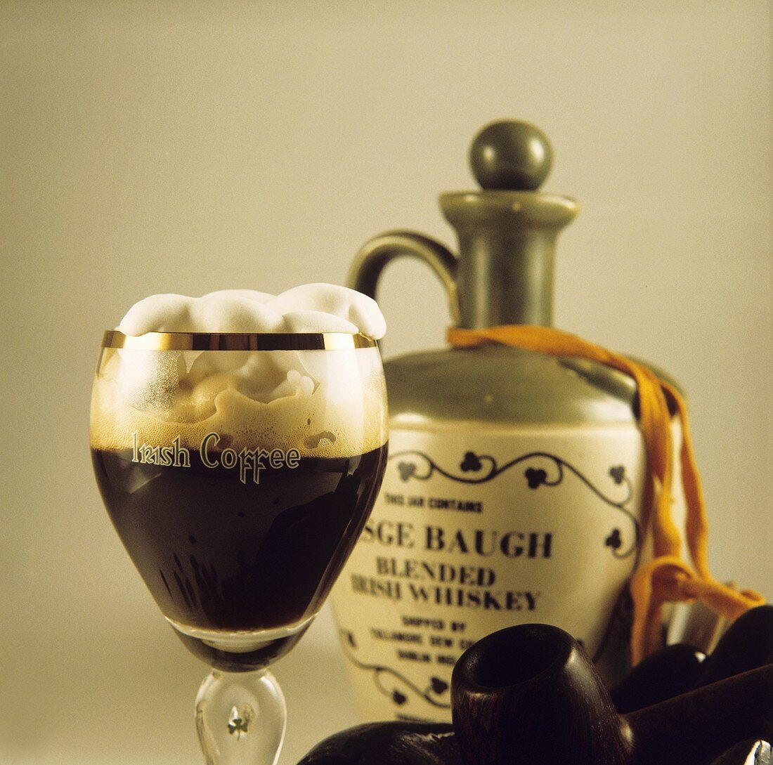 Irish Coffee im Glas, daneben Whiskey und zwei Pfeifen