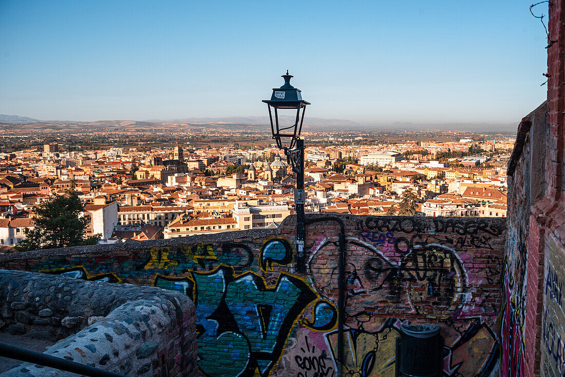 Mauern und Laterne vor der Silhouette von Granada bei Sonnenaufgang. Albaicin, Granada, Andalusien, Spanien