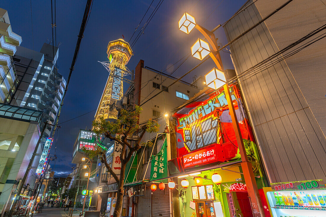 View of Tsutenkaku Tower and restaurants neon lights at dusk in the Shinsekai area, Osaka, Honshu, Japan