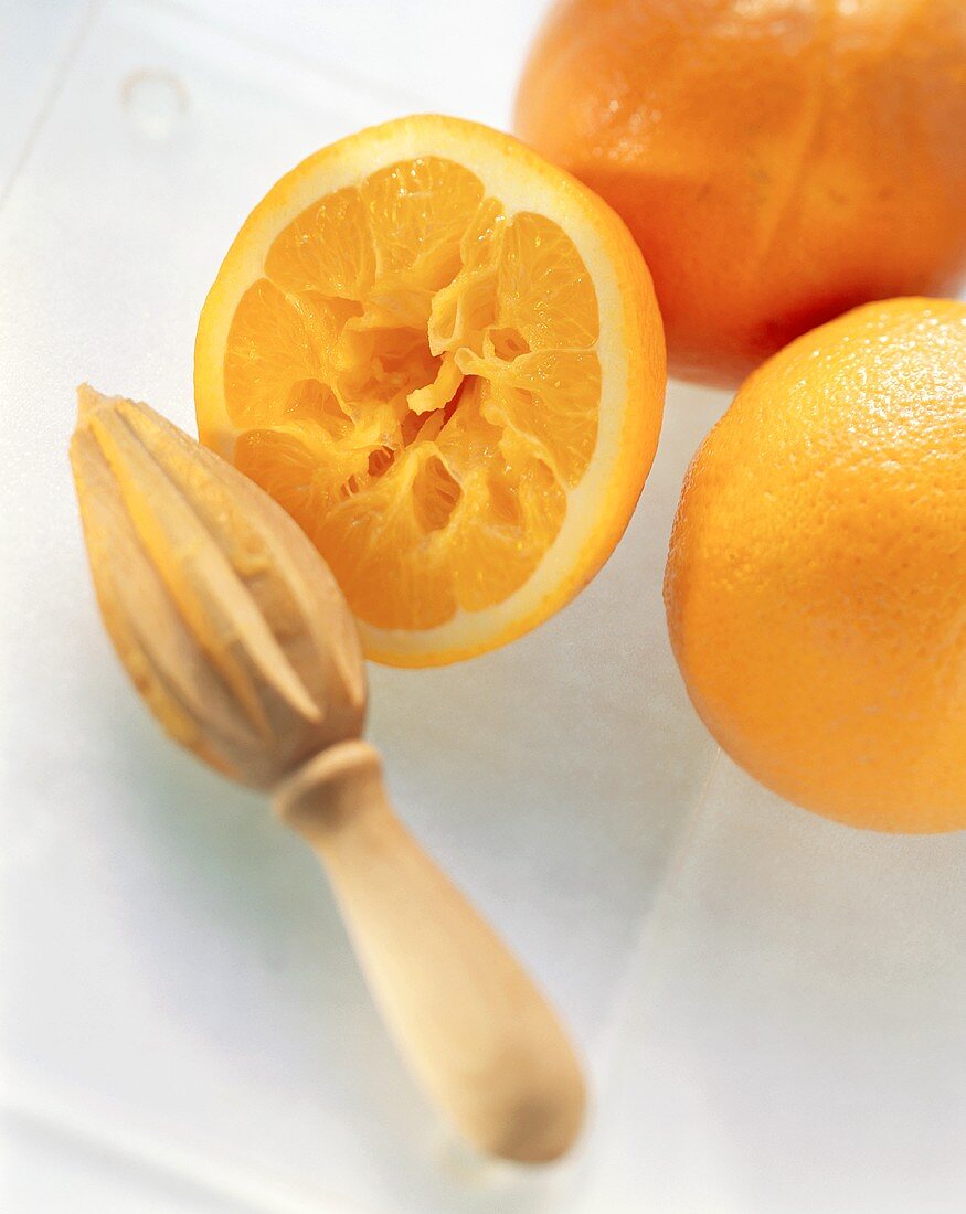 Orange half with wooden squeezer in front of whole oranges