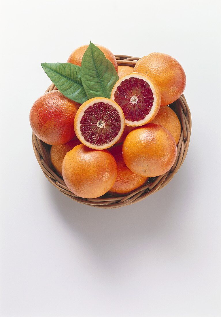 Whole blood oranges & two halves with leaves in basket