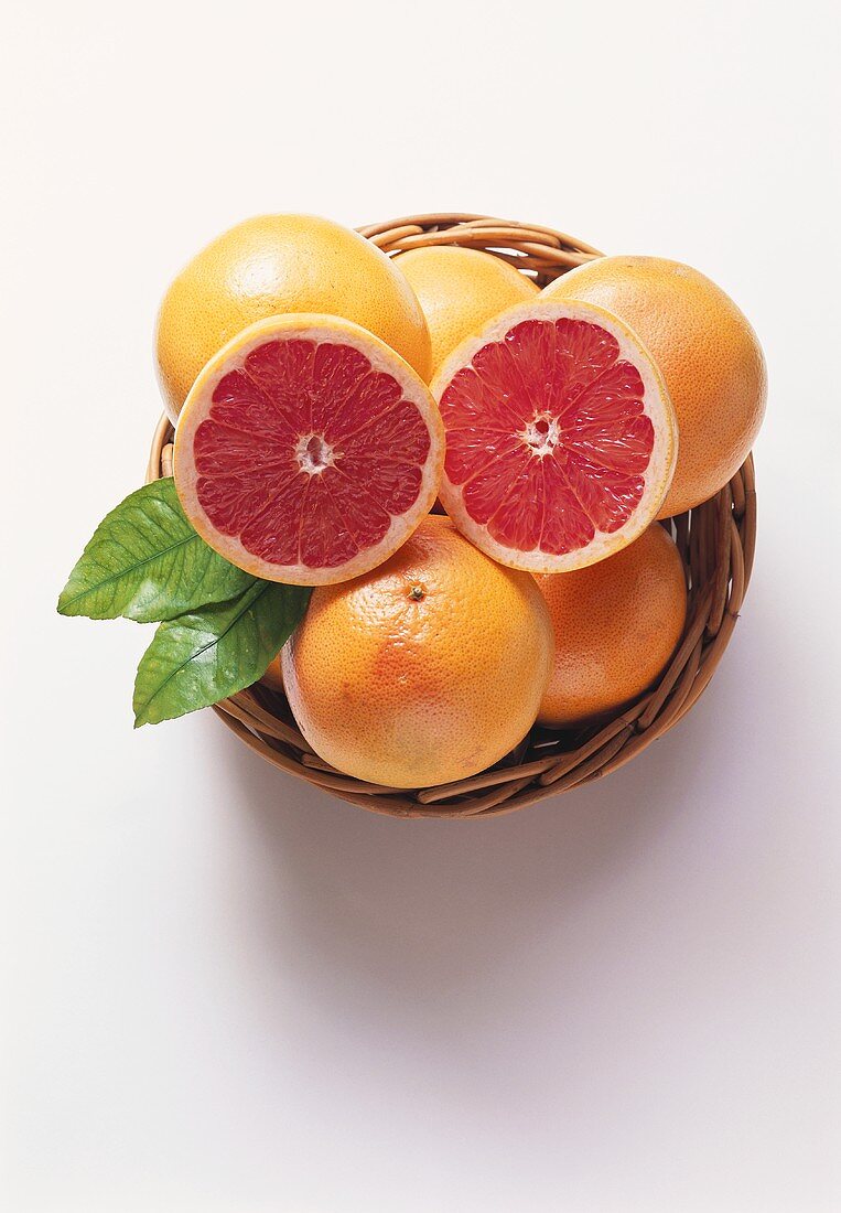 Two pink grapefruit halves on whole grapefruits in basket