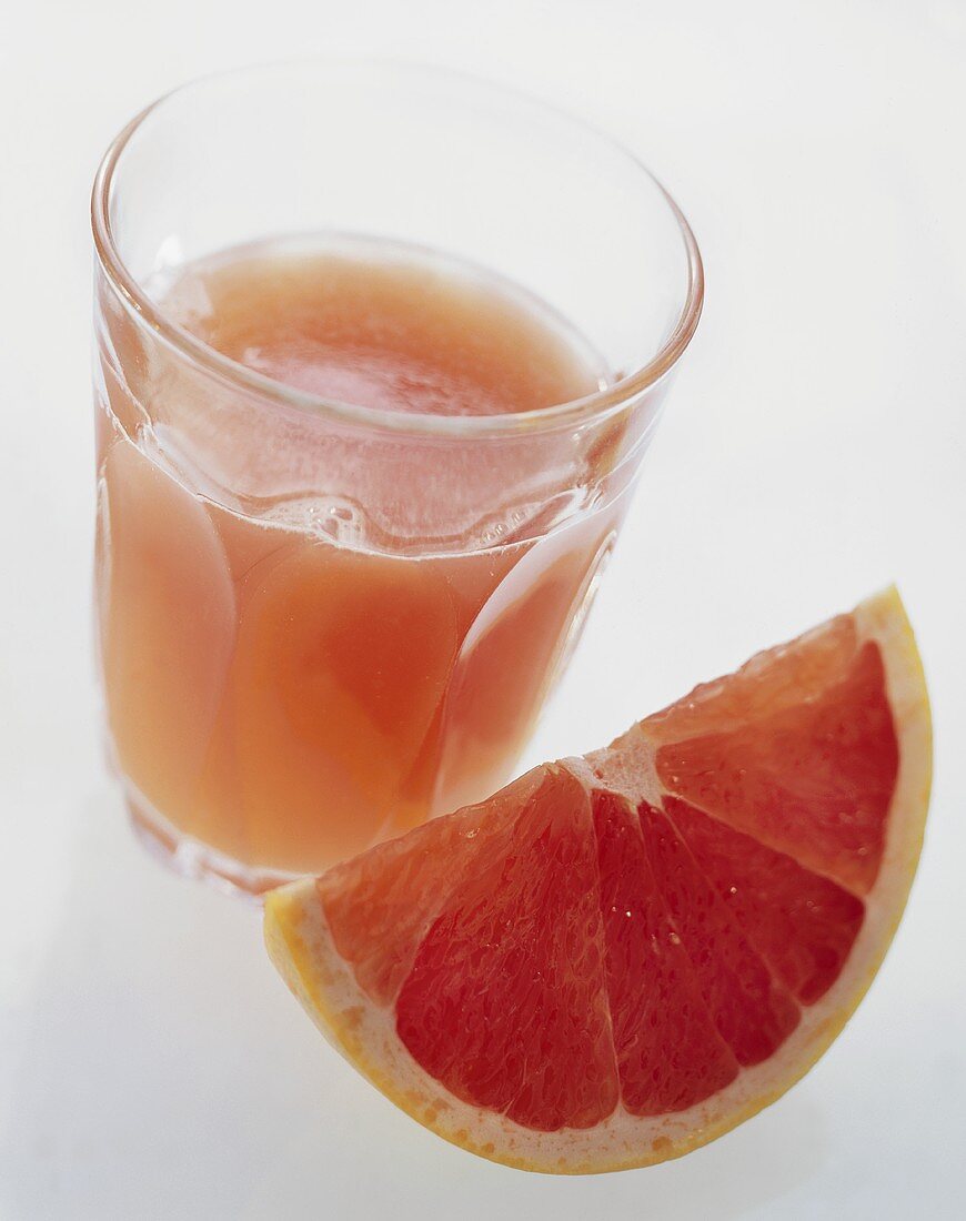 Rosa Grapefruitsaft im Glas, davor ein Grapefruitschnitz